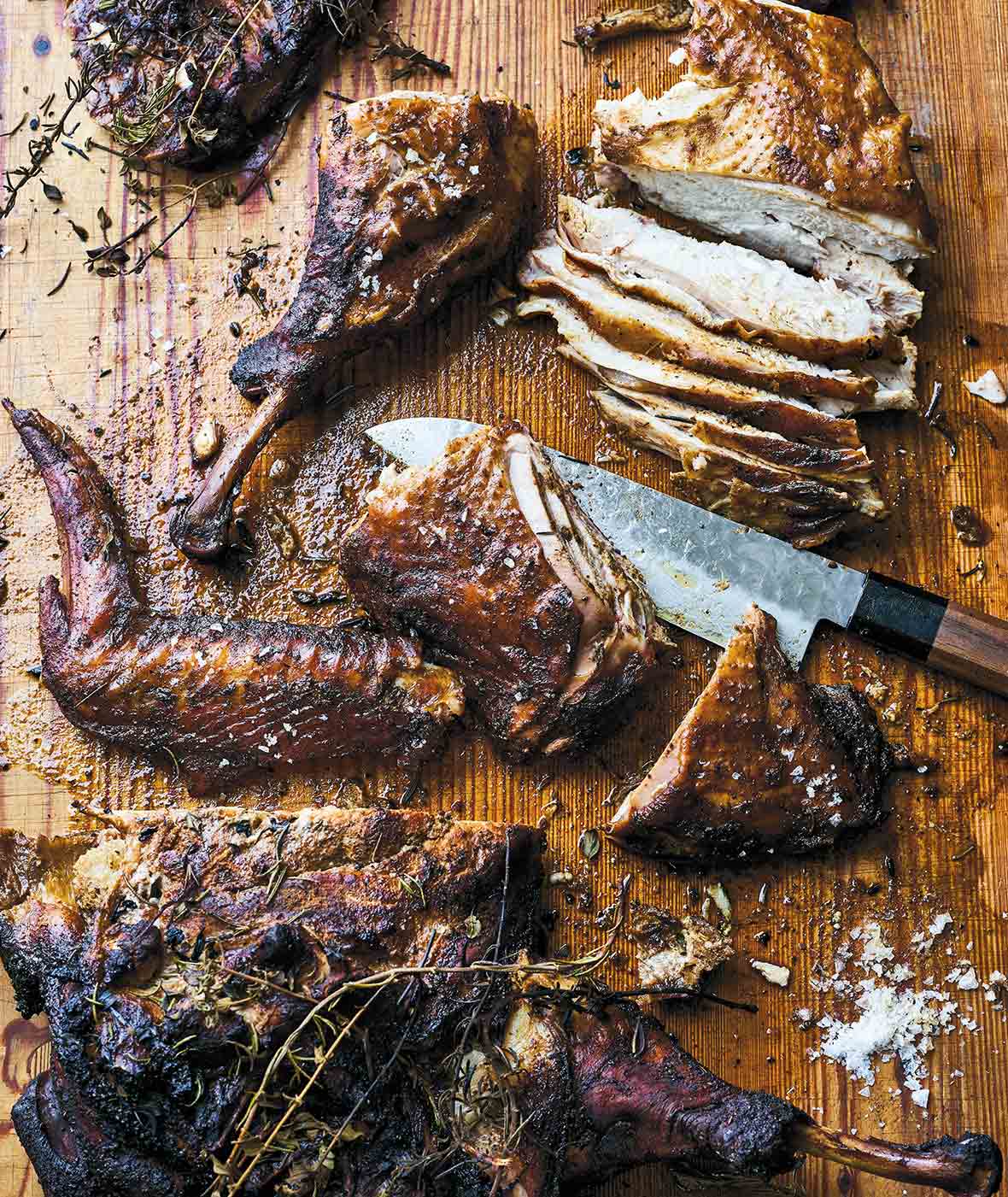 A Texas style smoked turkey cut into breast and leg pieces on a cutting board with a knife.