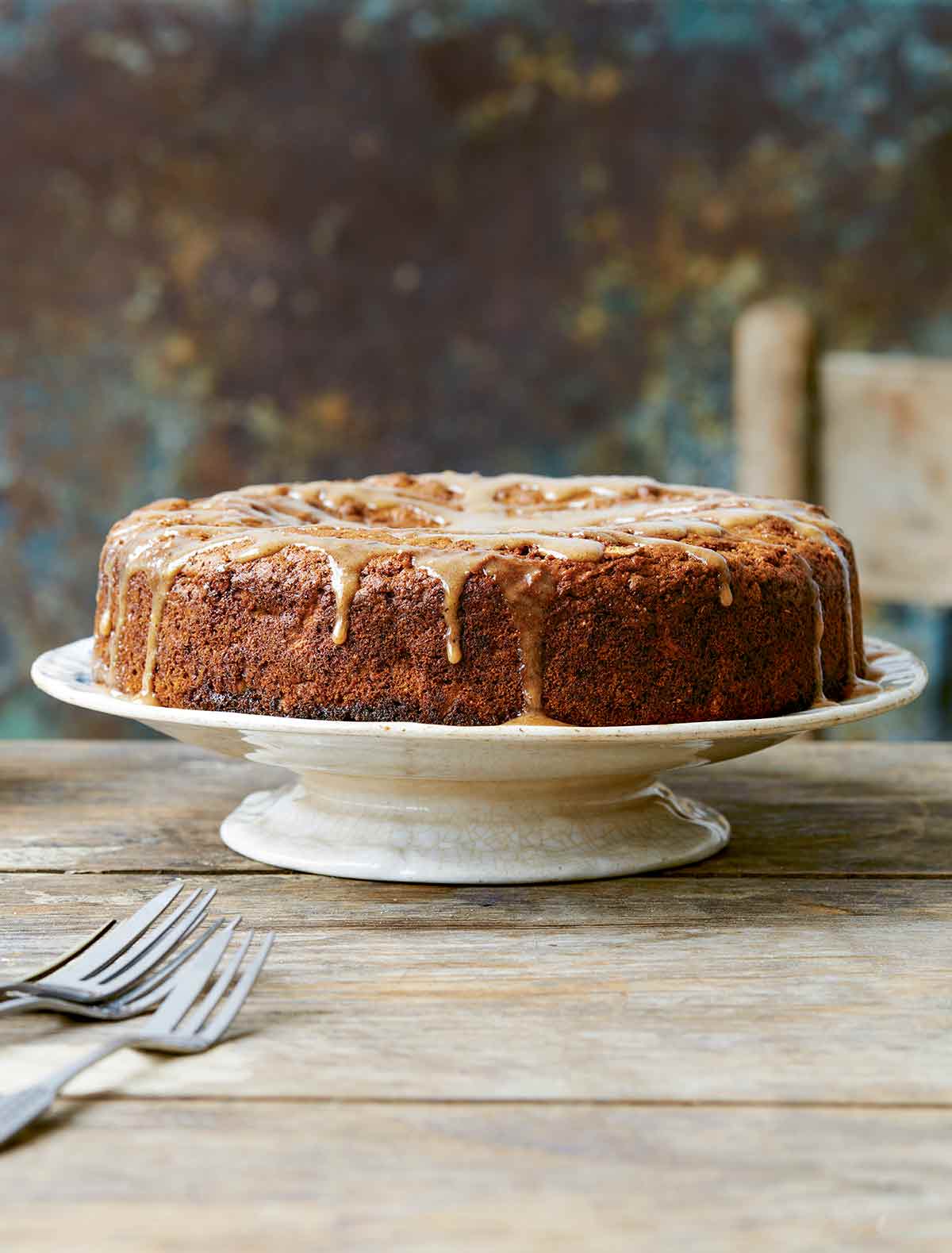 A vegan apple cake with chai drizzle on a white porcelain cake platter.