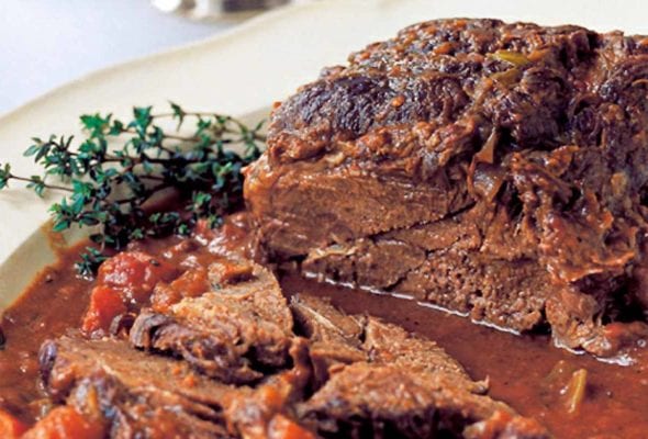 A partially sliced Barefoot Contessa company pot roast on a serving platter, garnished with thyme sprigs.