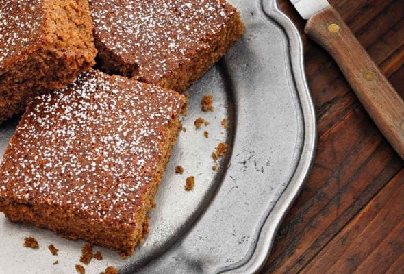 Squares of best homemade gingerbread cake dusted with confectioners' sugar on a silver platter.