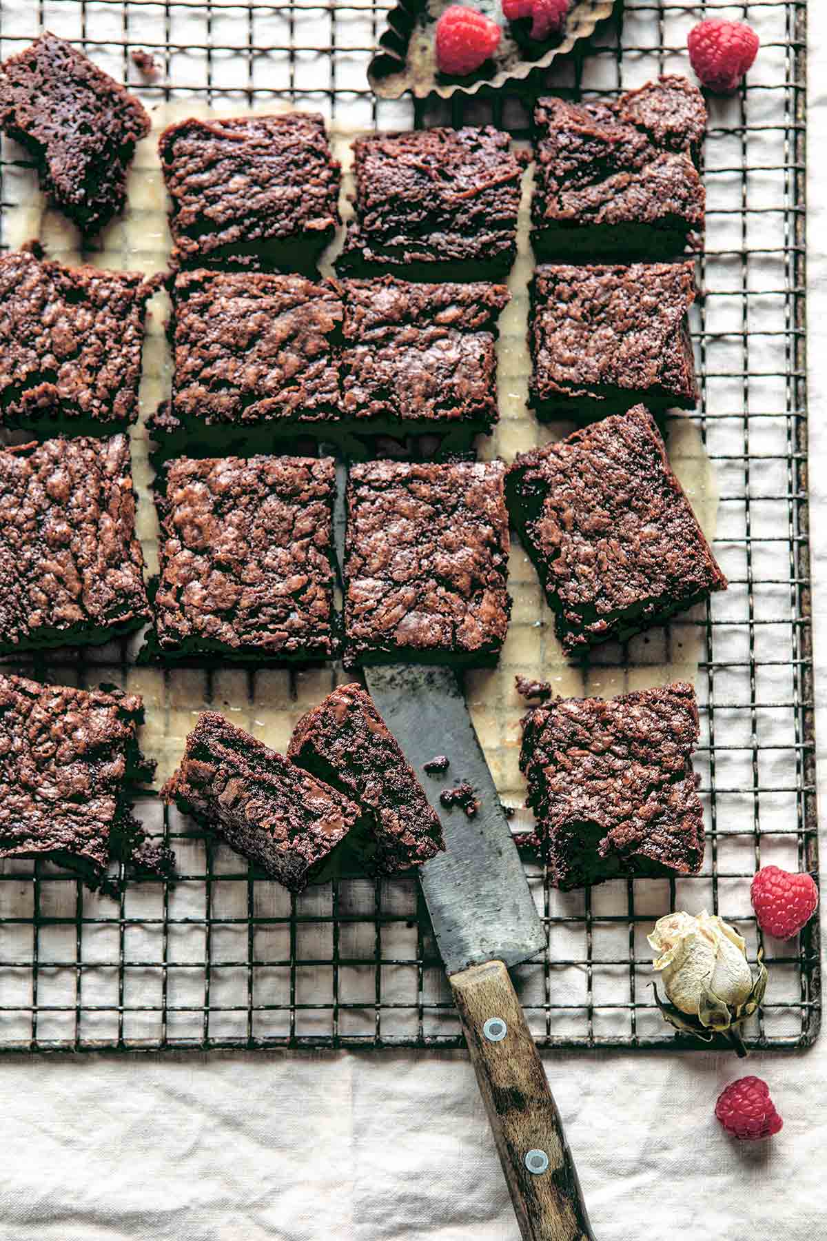A batch of five ingredient Nutella brownies cut into squares on a wire rack with fresh raspberries scattered around.