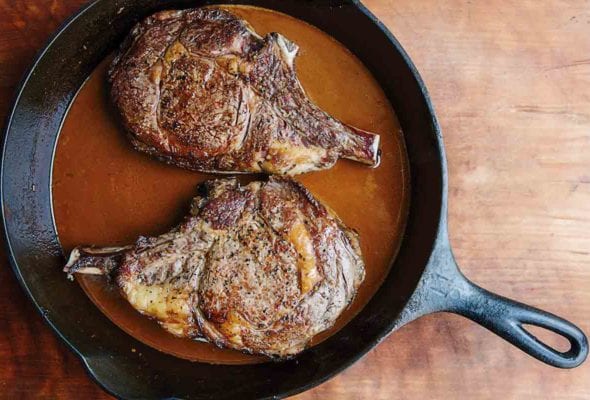 Two cowboy steaks in a cast-iron skillet with a Guinness sauce.