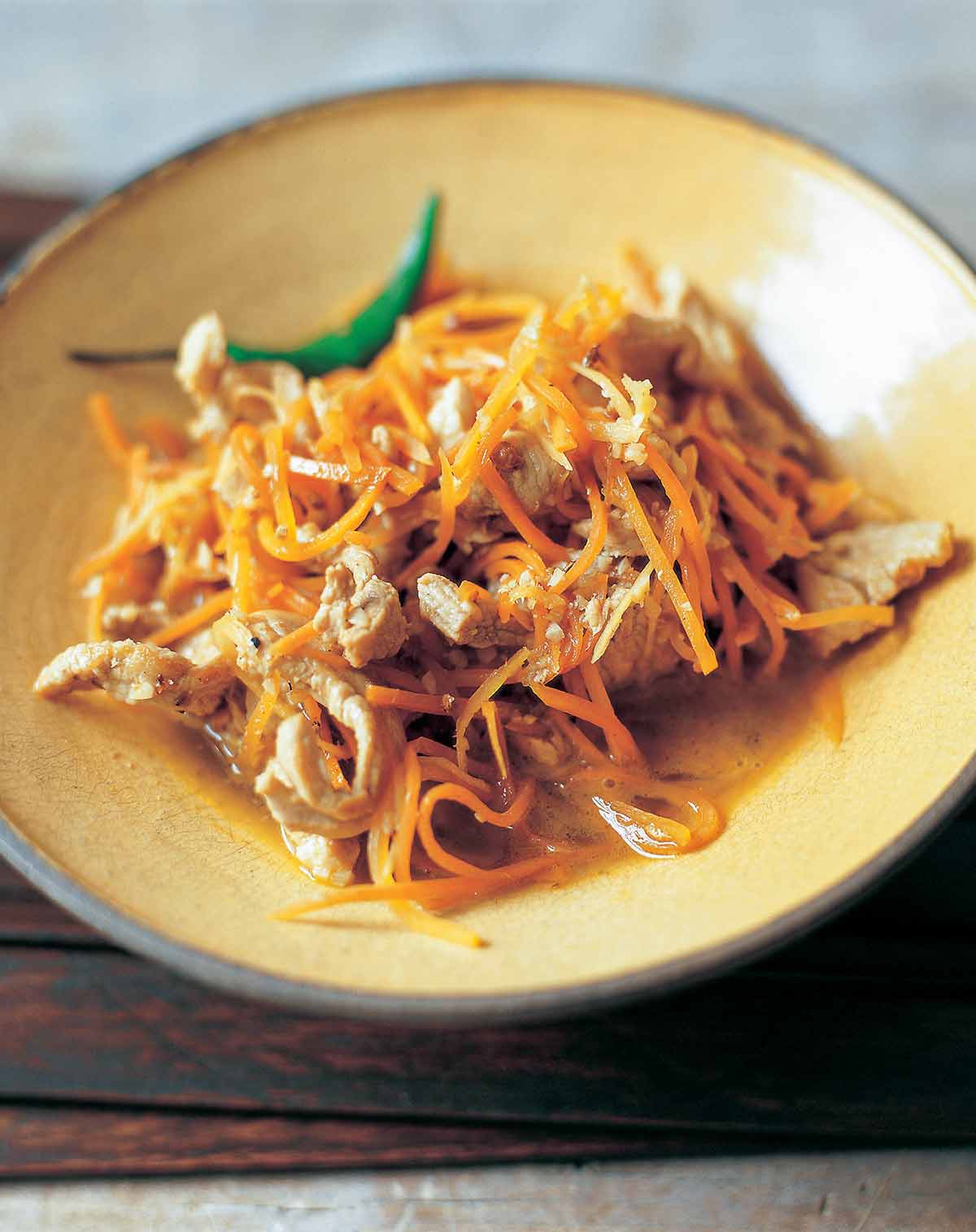 A brown bowl filled with ginger and carrot stir-fry on a wooden mat.