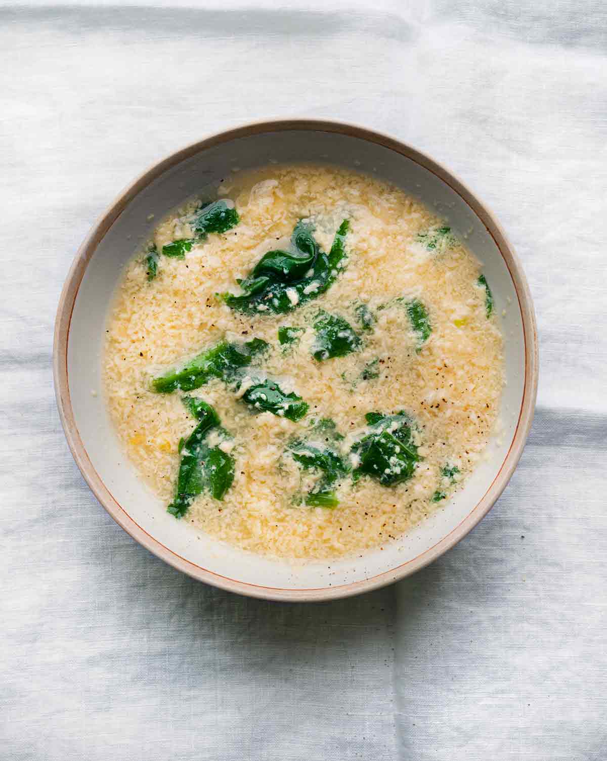 A bowl of Italian rag soup with wilted spinach on a white linen cloth.