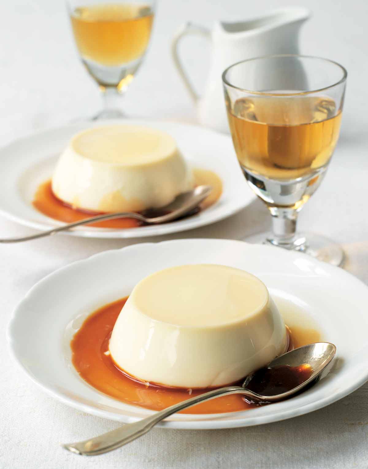 Two shallow bowls, each with an unmolded panna cotta in caramel, with a spoon resting in the bowl.