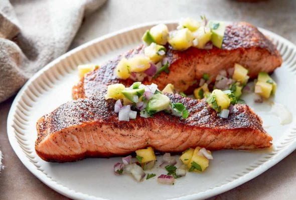Two pieces of blackened salmon topped with pineapple salsa on an oval serving plate.