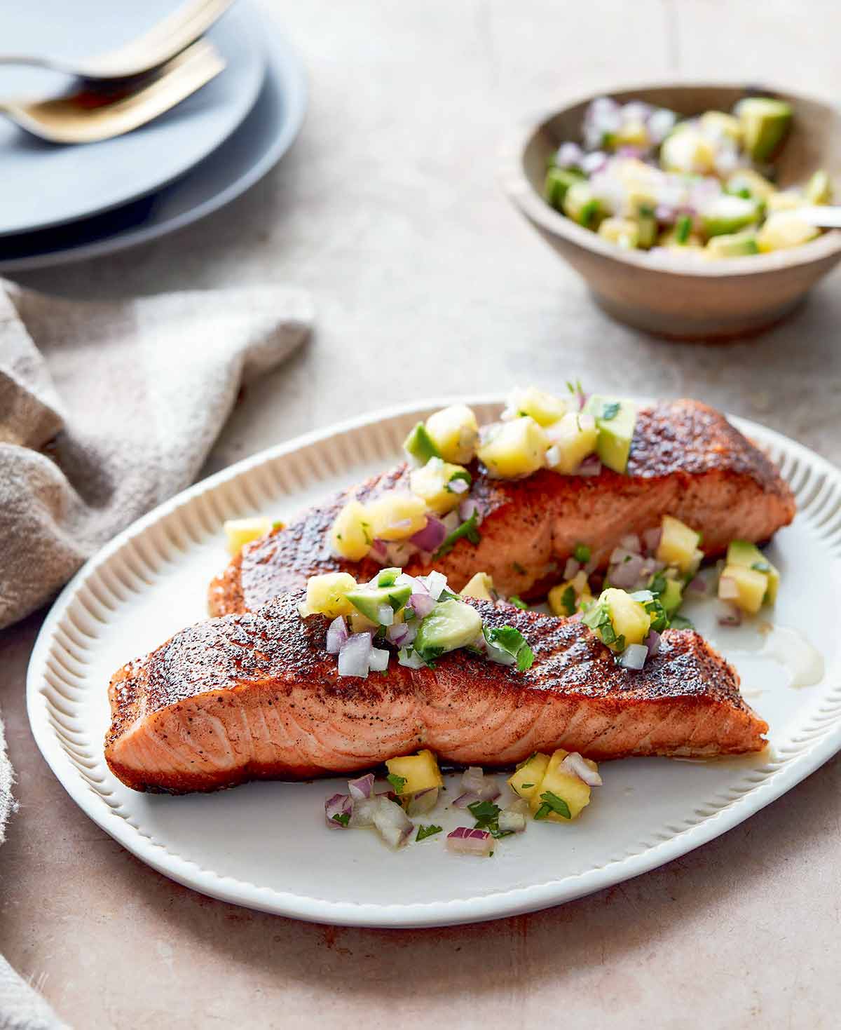Two pieces of blackened salmon topped with pineapple salsa on an oval serving plate.