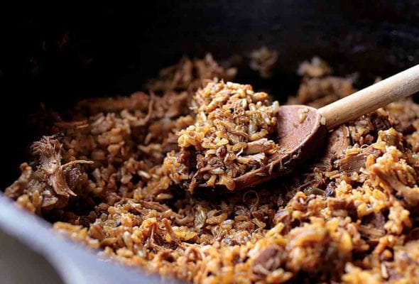 A cast-iron pot of Cajun Chicken and Sausage Jambalaya with a wooden spoon resting inside.