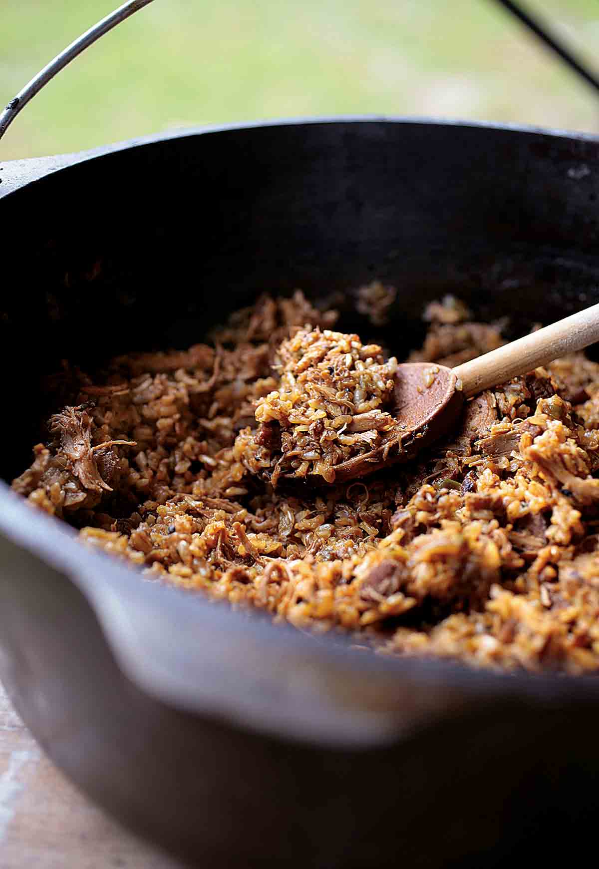 A cast-iron pot of Cajun Chicken and Sausage Jambalaya with a wooden spoon resting inside.