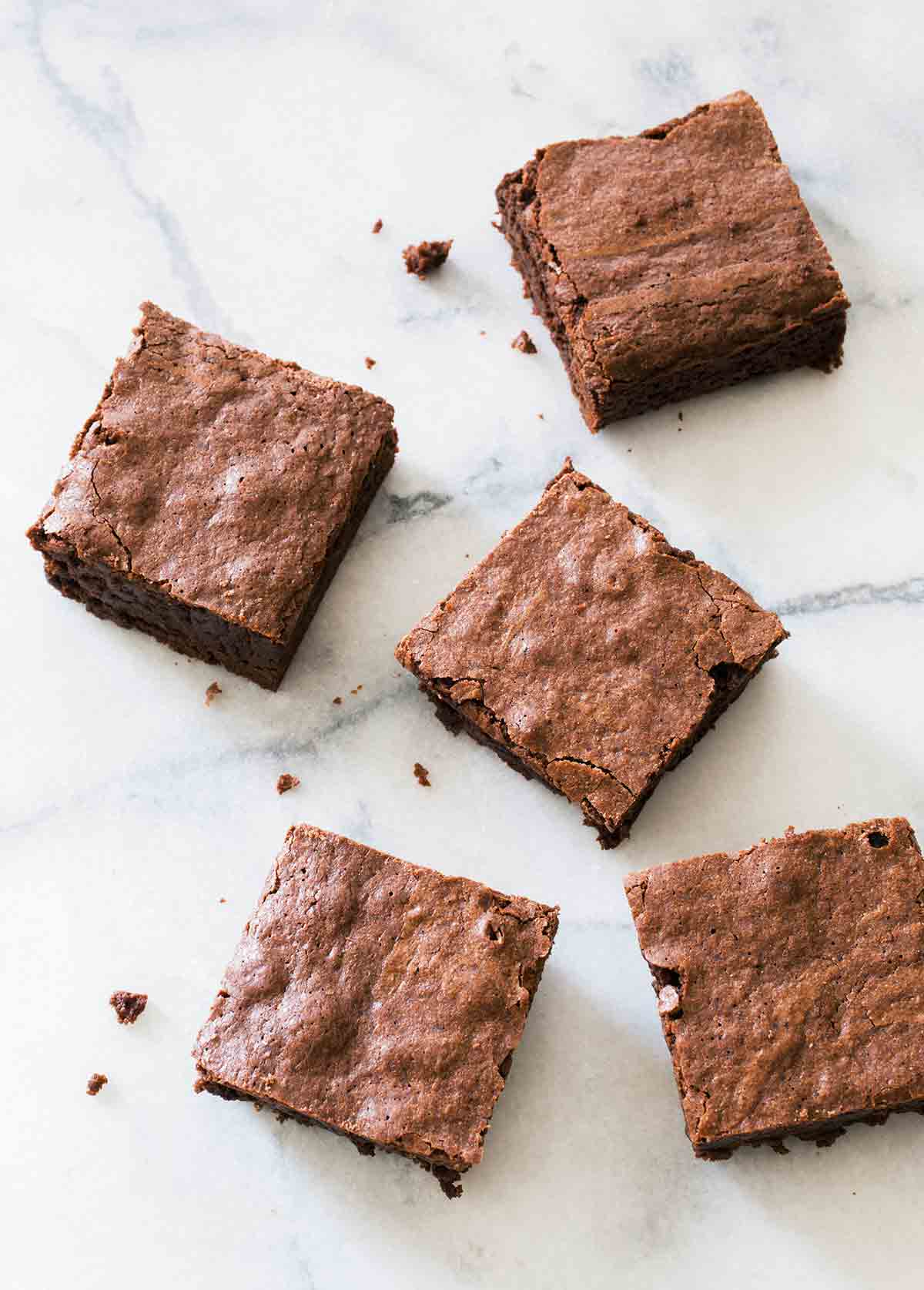 Squares of chocolate chip brownies on a white marble surface.