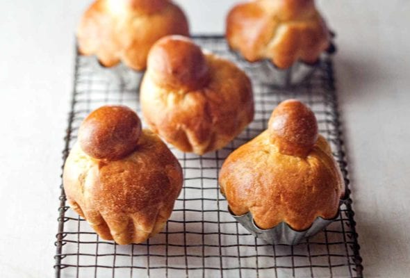 Five classic brioche rolls on a wire rack, three in metal tins, two removed from the tins.