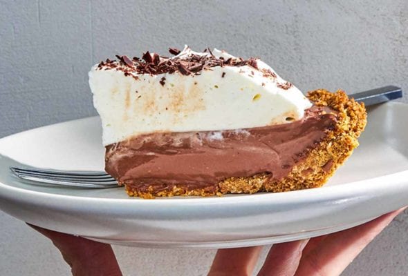 A person holding a white plate with a slice of dark chocolate pudding pie and a fork.