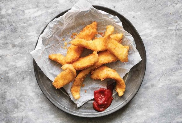 A pile of fancy fish sticks on a piece of parchment with a dollop of ketchup beside them.