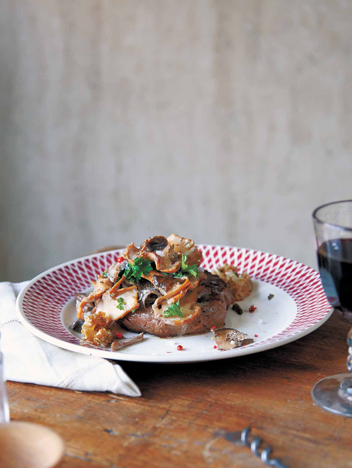 A red and white plate topped with a filet mignon and wild mushrooms sauce.
