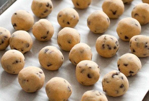 Balls of frozen chocolate chip cookie dough on a parchment-lined baking sheet.