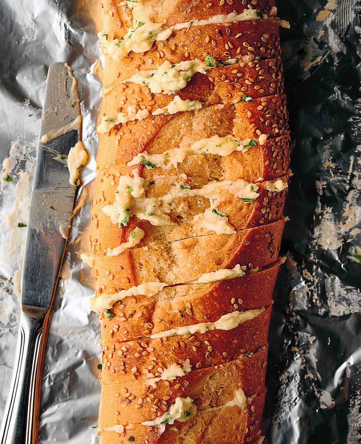 A loaf of garlic bread, cut into deep slices and covered in garlic butter on a piece of aluminum foil.