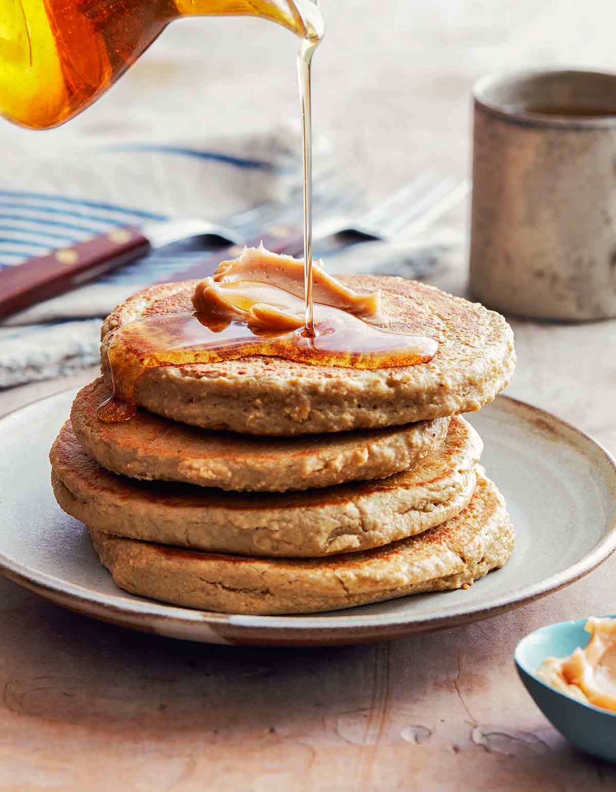 A stack of four gluten-free banana oat pancakes with syrup being poured over the top.