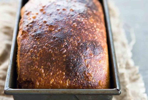 A browned loaf of homemade sandwich bread in a metal loaf tin.