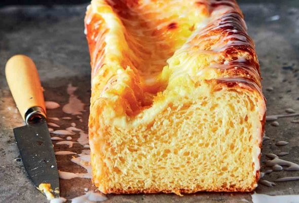 A loaf of lemon cream cheese Danish bread on a piece of foil with a knife lying beside it.