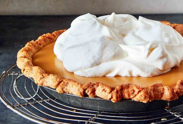 A whole maple cream pie, topped with whipped cream on a round wire rack.