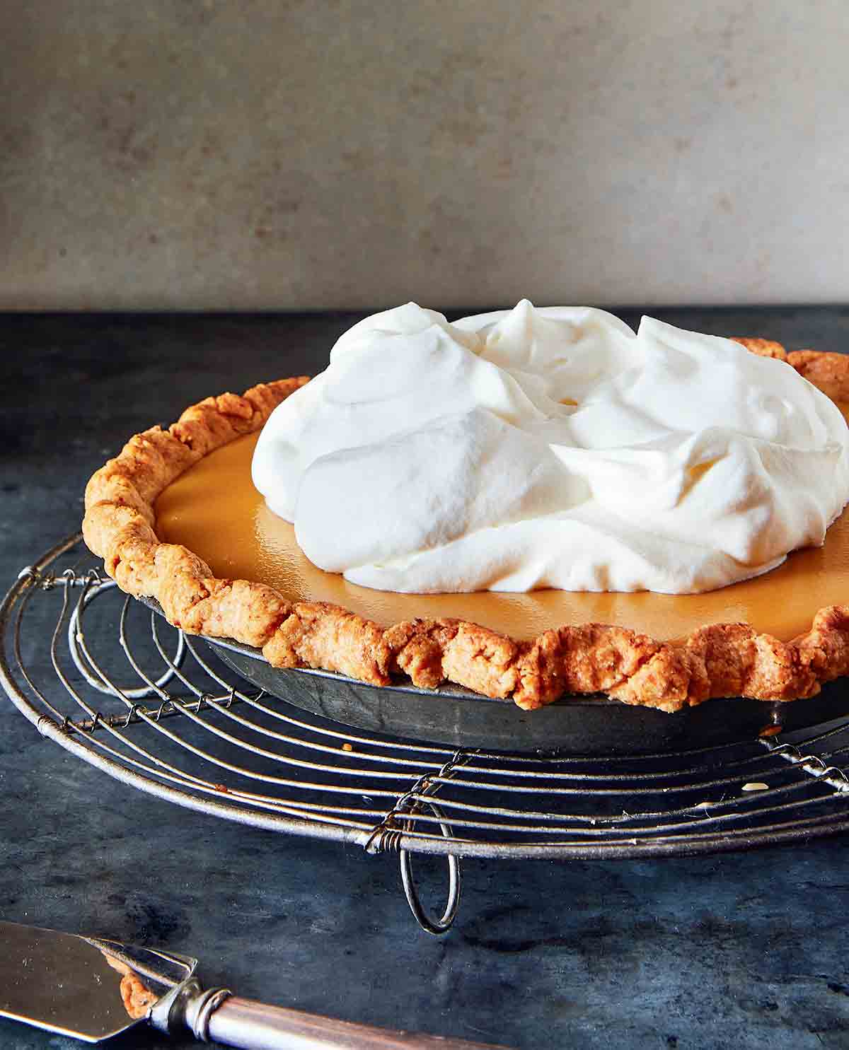 A whole maple cream pie, topped with whipped cream on a round wire rack.