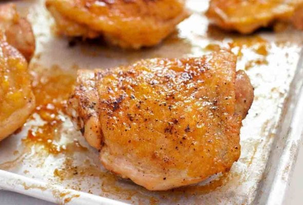 Sheet pan of oven-roasted chicken thighs, topped with salt and pepper.