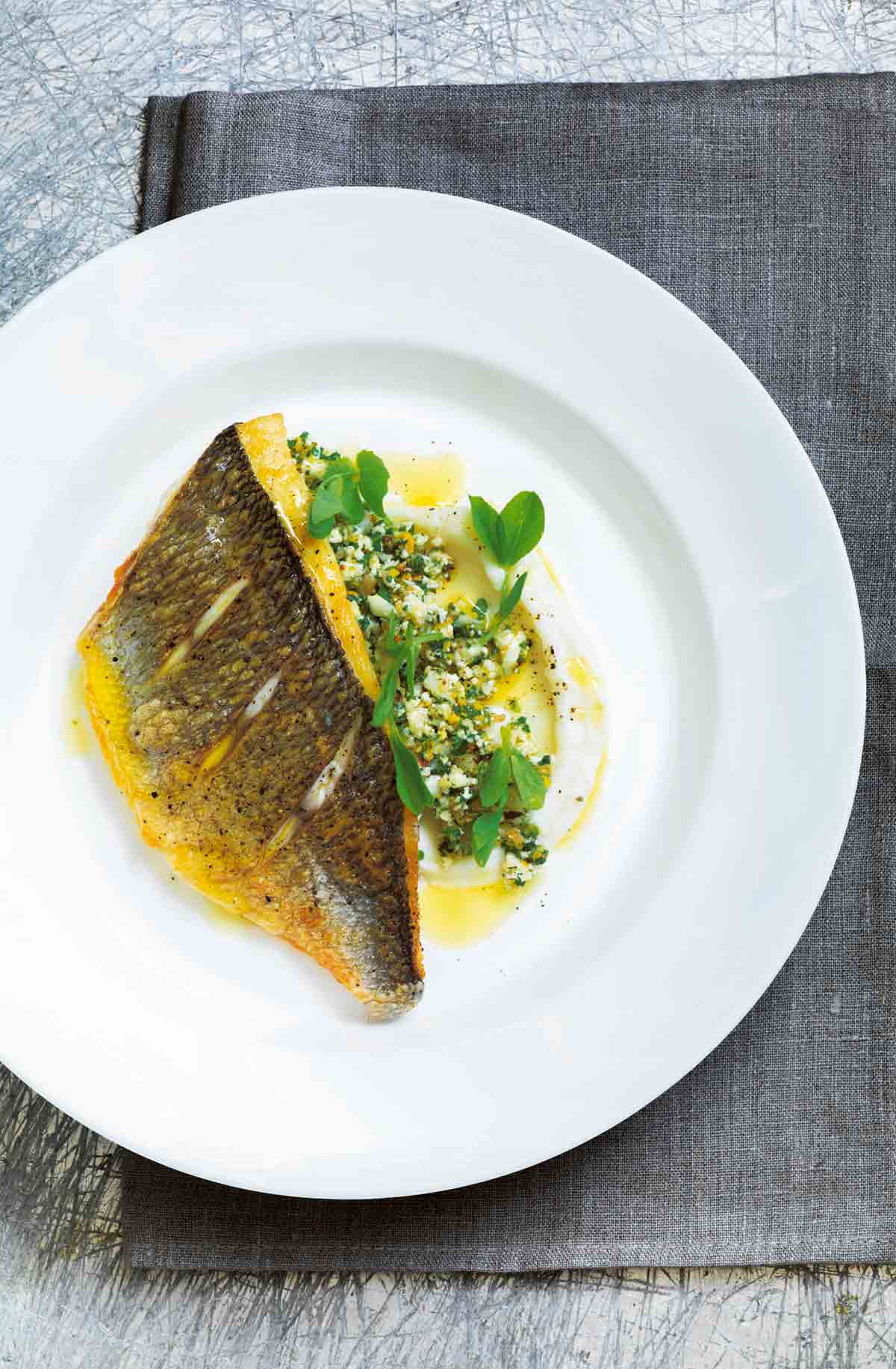 A piece of pan-fried fish on top of cauliflower "couscous" and cauliflower puree on a white plate.