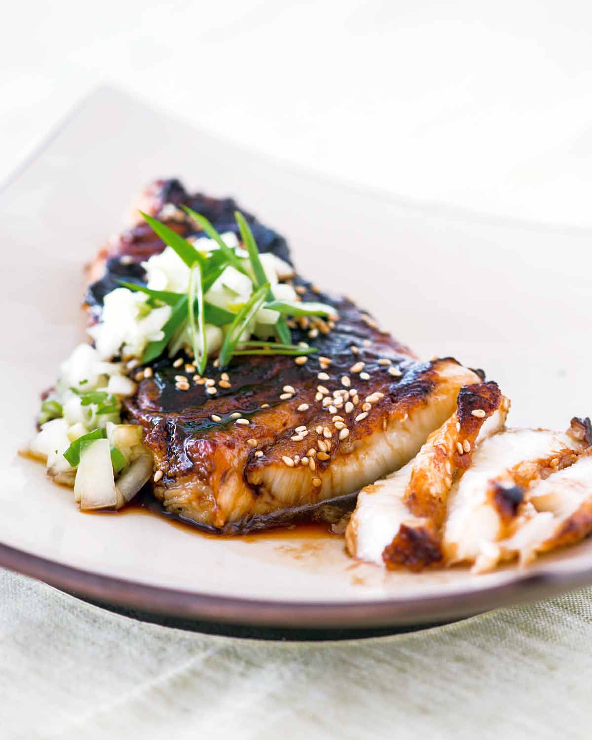 A piece of sea bass topped with soy glaze and cucumber salsa on a square shaped white plate.