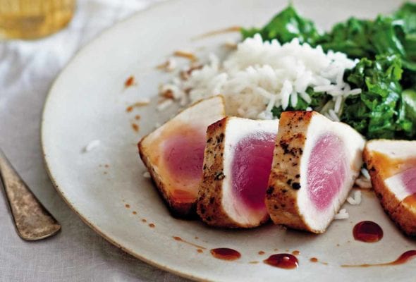 A white plate with four slices of seared tuna with sweet and sour sauce, rice, and cooked greens.