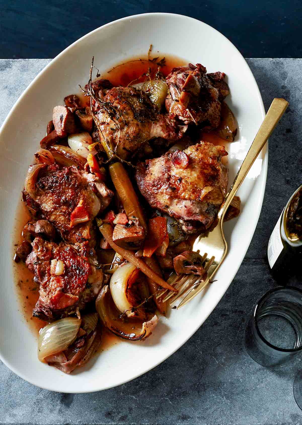 A white oval serving plate filled with slow cooker coq au vin and a gold fork resting on the side of the plate.