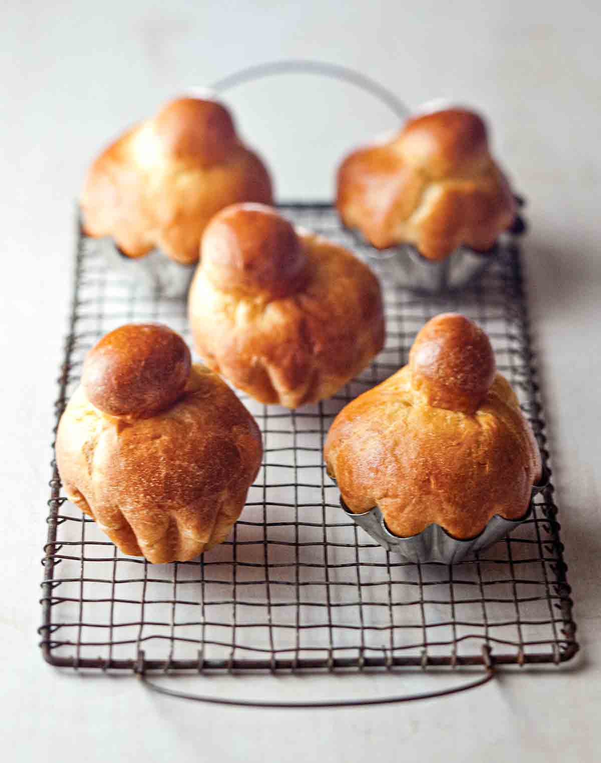 Five classic brioche rolls on a wire rack, three in metal tins, two removed from the tins.