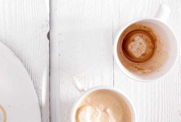 Two mugs, one empty and the other filled with Irish coffee on a white wooden table.