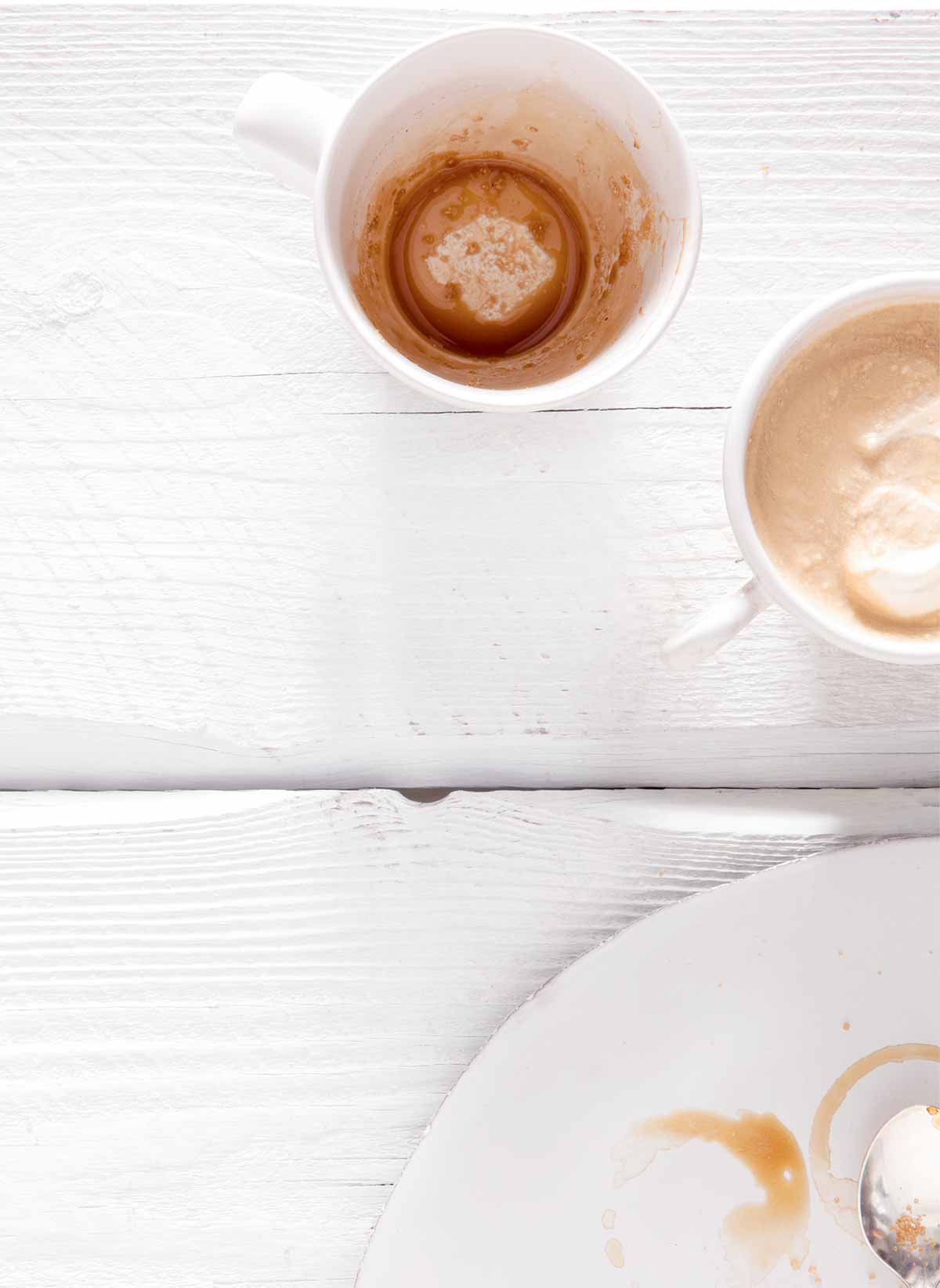 Two mugs, one empty and the other filled with Irish coffee on a white wooden table.