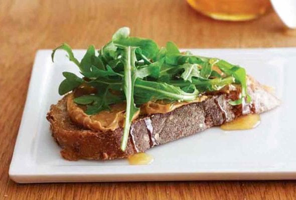 A peanut butter, honey, and arugula sandwich on a white plate.