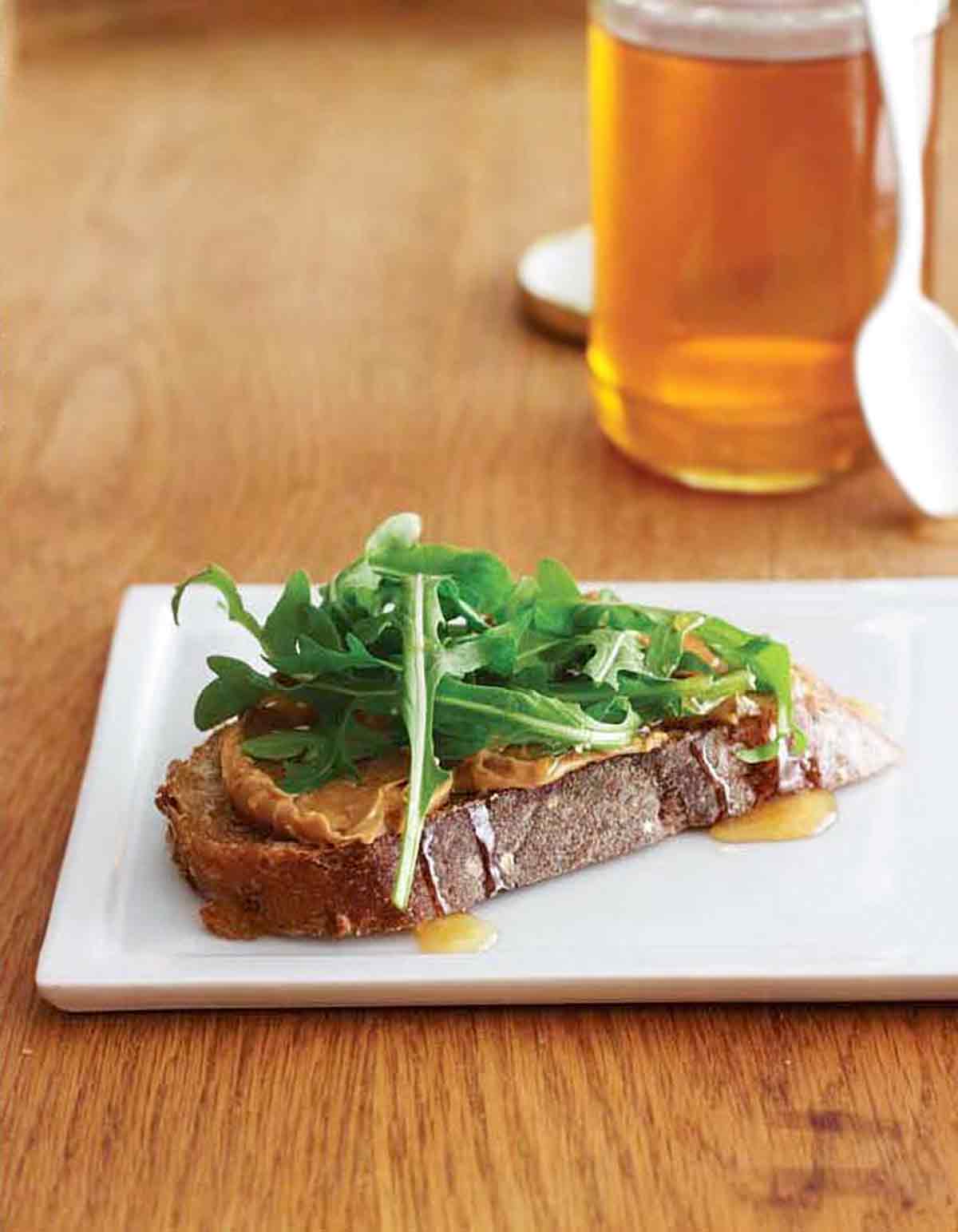 A peanut butter, honey, and arugula sandwich on a white plate.