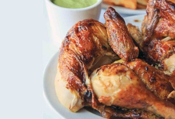Pieces of Peruvian chicken on a platter with a cup of aji verde in the background.