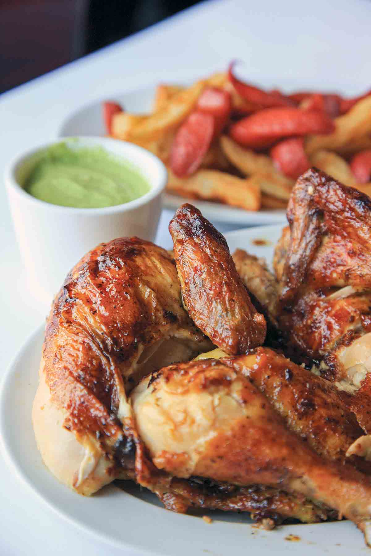 Pieces of Peruvian chicken on a platter with a cup of aji verde in the background.
