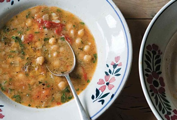 Two bowls, one filled with smoked paprika and chickpea soup, with a spoon resting inside, and the other bowl empty.