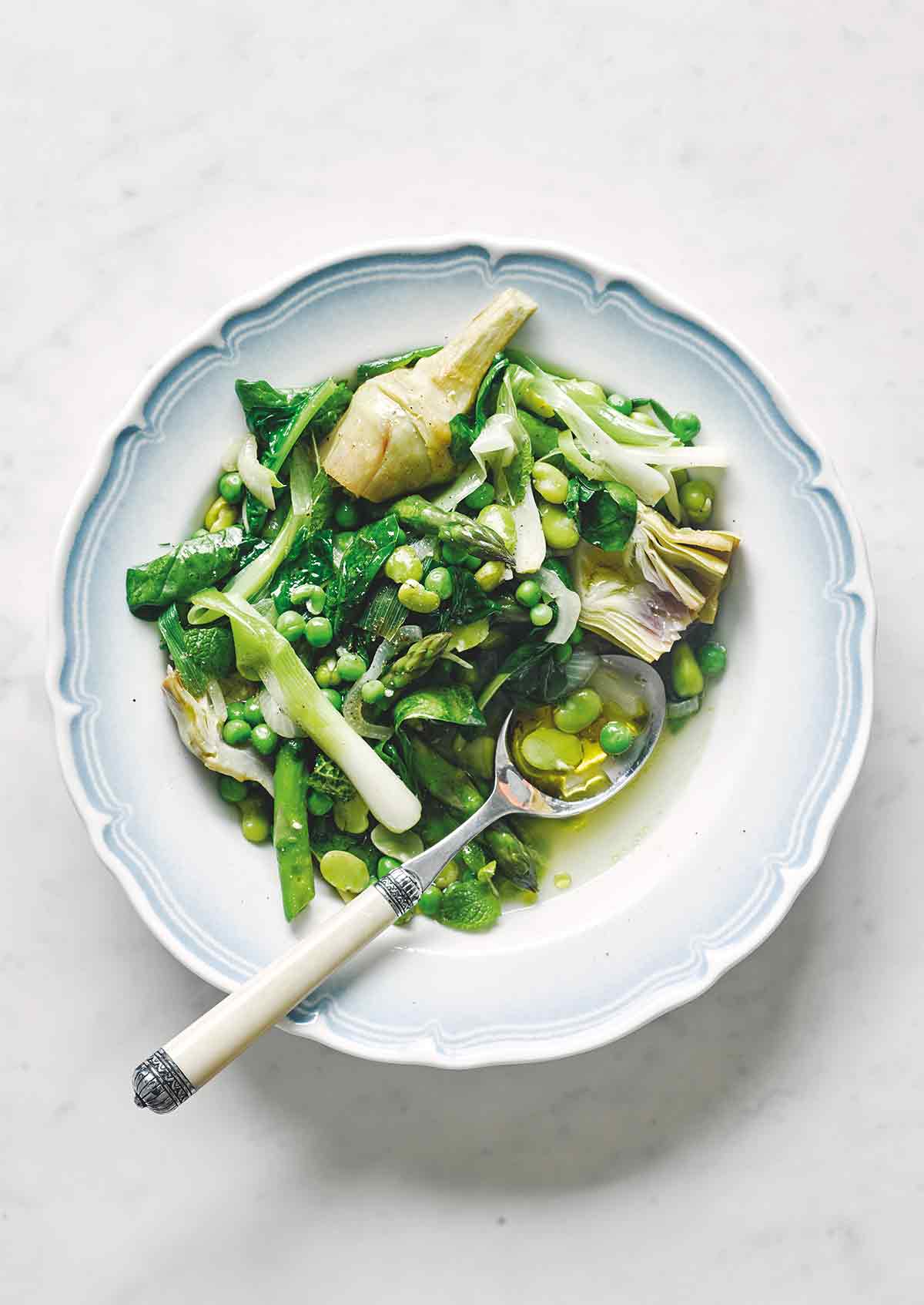 A white and blue bowl filled with spring vegetable stew with a spoon resting in the bowl.