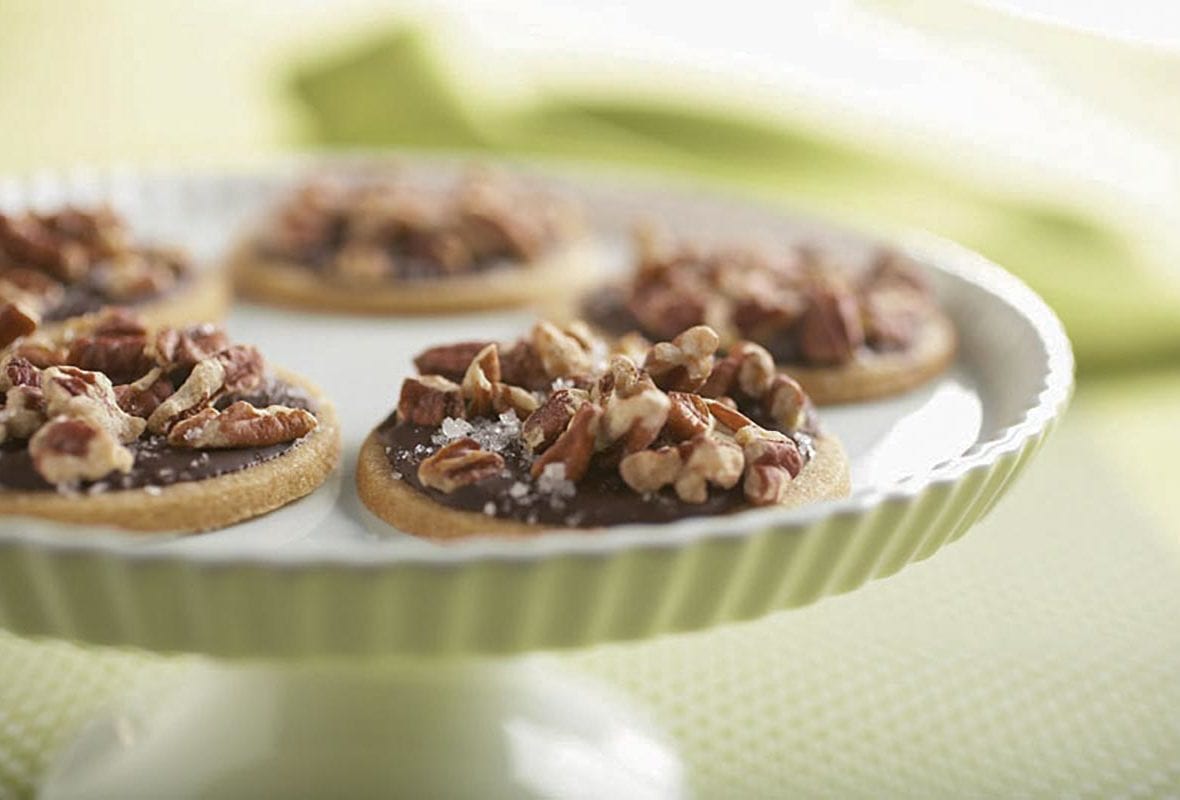 Five toffee cookies with dark chocolate glaze on a cake stand.