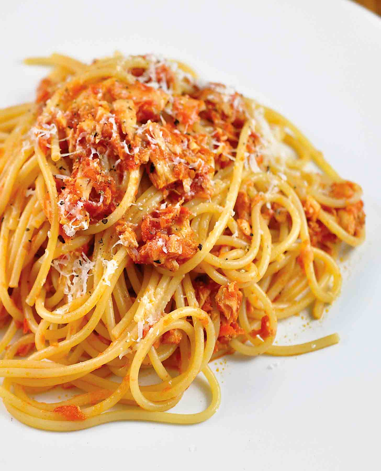 A tangle of tomato and tuna spaghetti on a white plate.