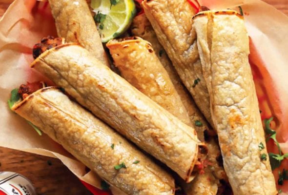 A basket of black bean taquitos with lime halves and hot sauce on the side.