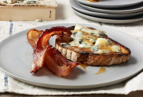 A piece of blue cheese tartine with two slices of crispy bacon on a grey plate.