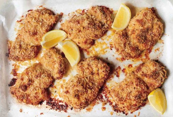 Six breaded oven fried chicken thighs with four lemon wedges in a parchment-lined dish.