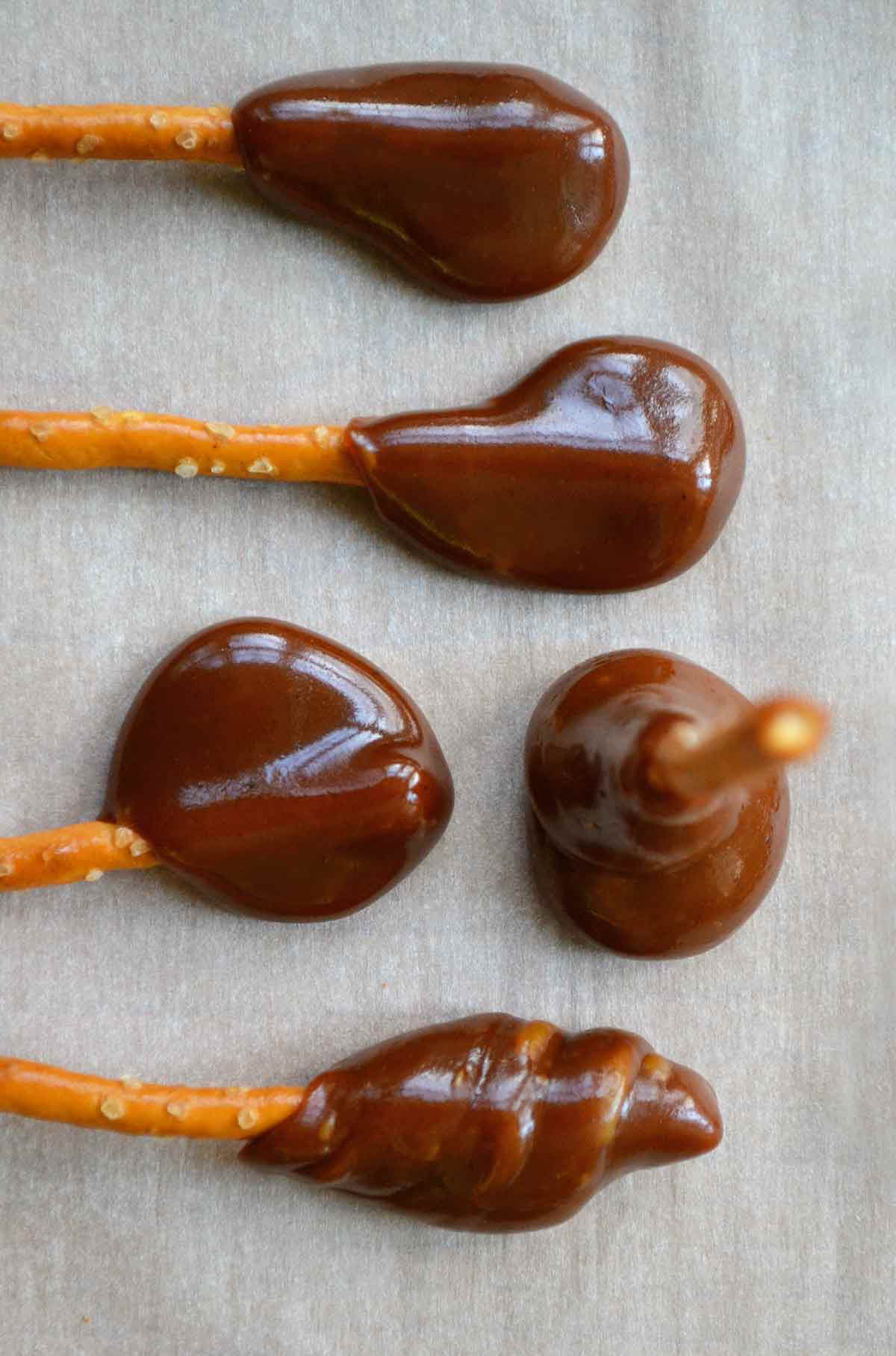 Five caramel-dipped pretzel sticks on a sheet of parchment paper.