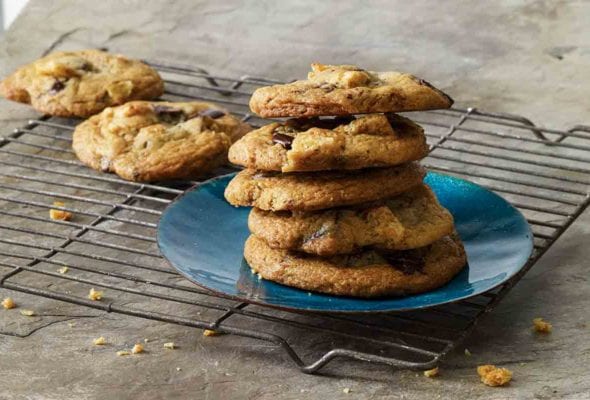 A stack of chicharron chocolate chip cookies on a blue plate on a wire rack with a couple more cookies on the rack.