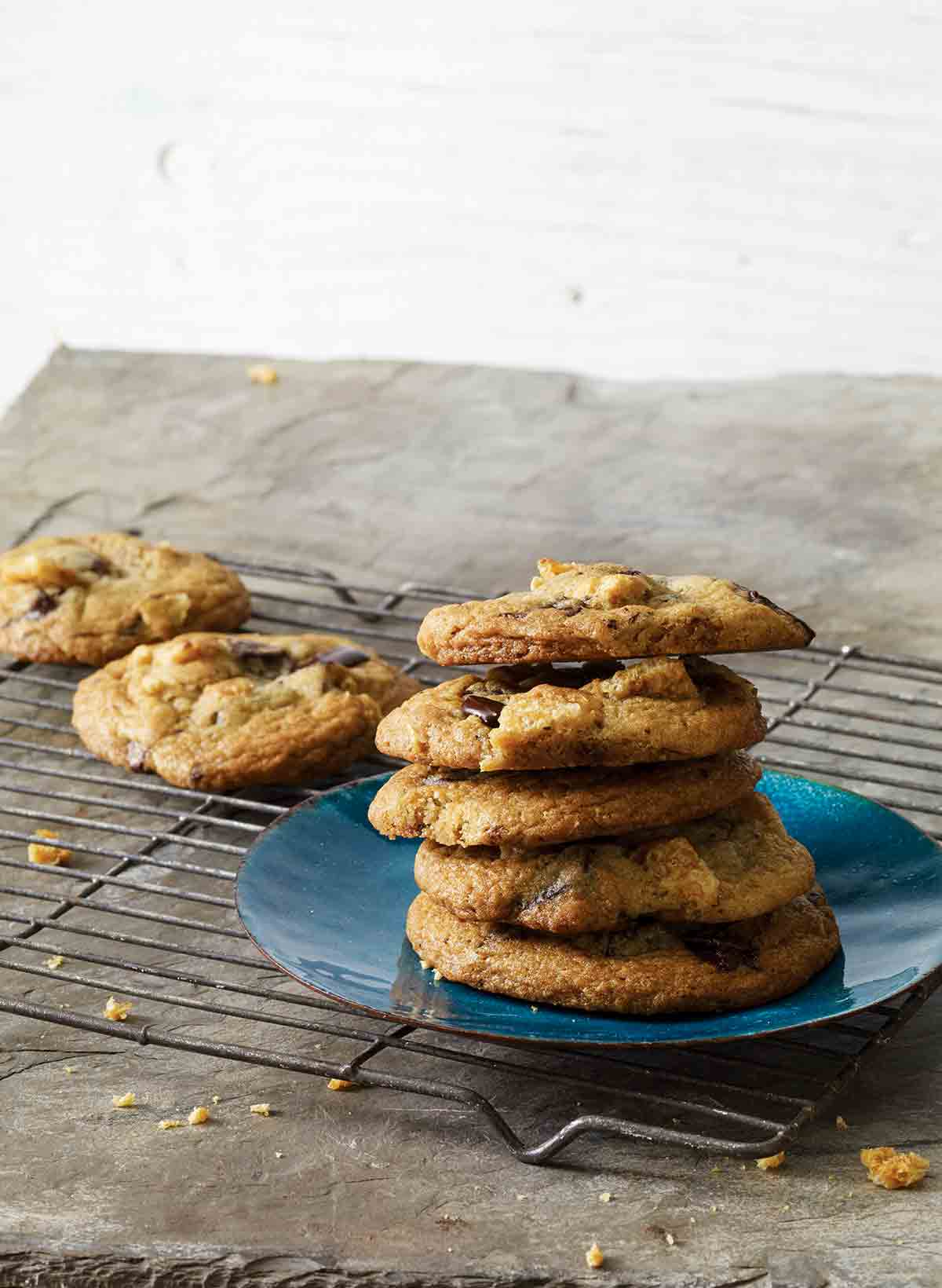 A stack of chicharron chocolate chip cookies on a blue plate on a wire rack with a couple more cookies on the rack.