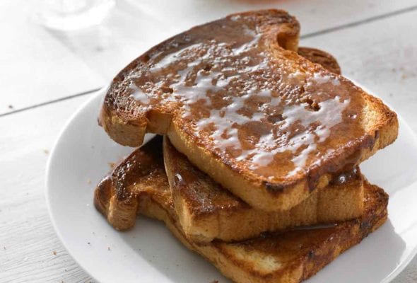 Three slices of cinnamon toast stacked on a white plate.