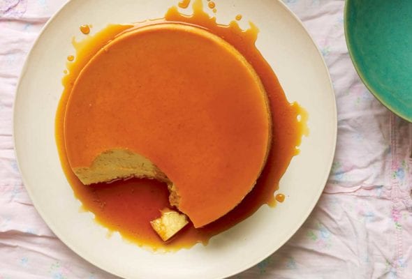 A classic flan de leche on a white plate, covered with caramel and a spoonful of custard missing from the flan.