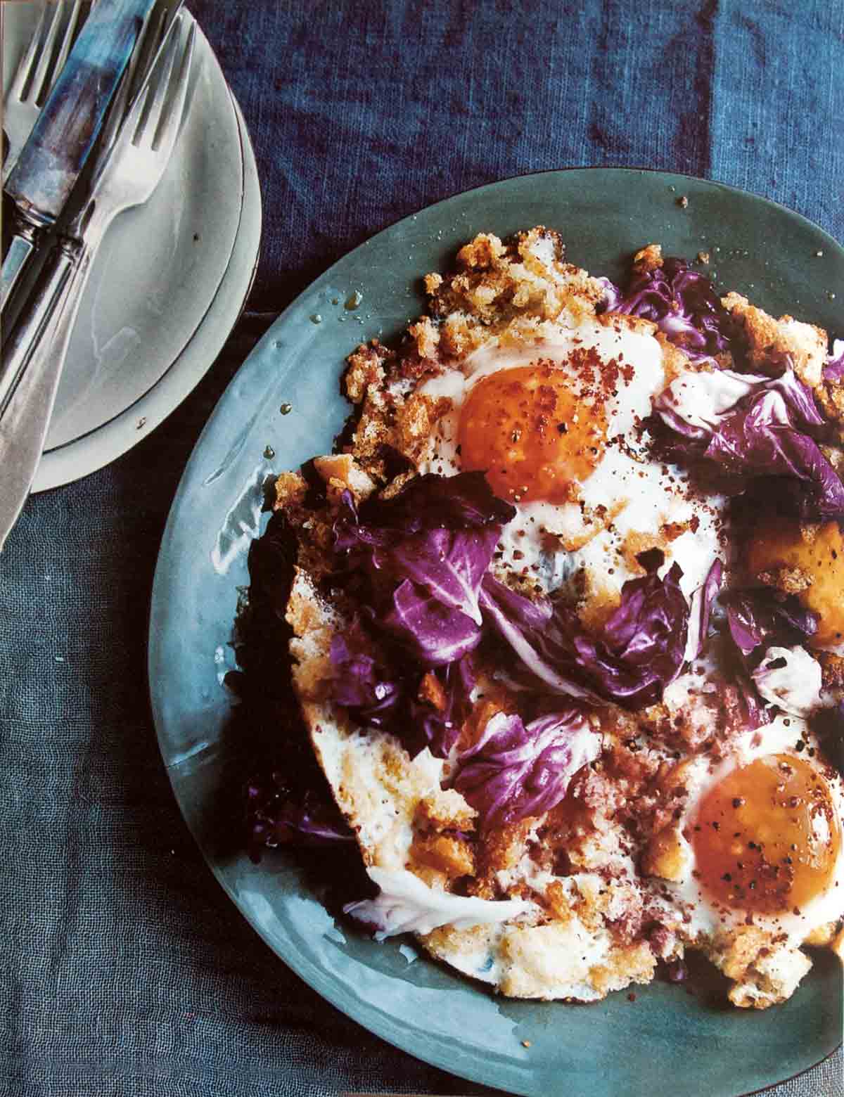 A blue plate topped with two fried eggs with crisp bread crumbs and radicchio.